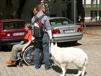 Tanja im Rollstuhl mit  2 Helfern und Hund