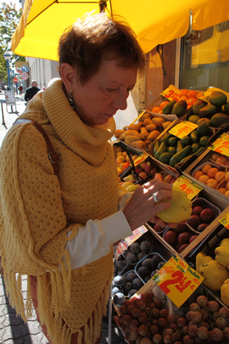 Margit beim Einkaufen am Obststand, sie betastet das Obst