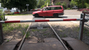 Schranke, dahinter quert ein Auto den Schienenstrang, dahinter wieder Schranke.