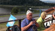 Josef und Silvia an einem Biertisch, im Hintergrund der See