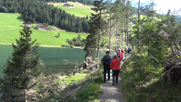 Pitschedabber wandern am See entlang, von hinten gesehen. Links auf den Bergen Almen