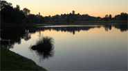 Blick über den nach dem Sonnenuntergang vom rötlichen Himmel rötlich gefärbten See auf das dunkle Ufer