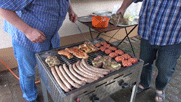 Blick auf den Grill. Darauf liegen Würstchen, Steaks, Hackfleischbällchen