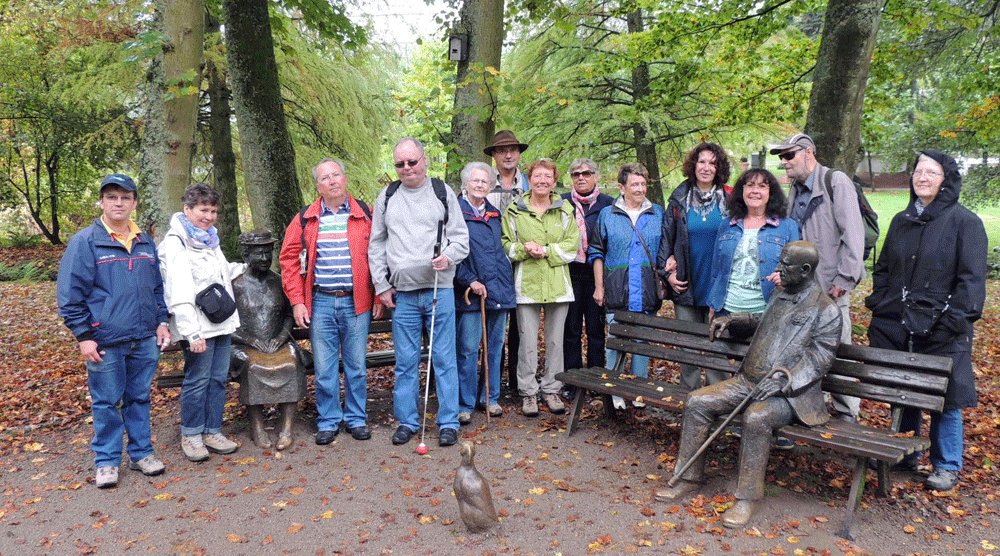 die Pitschedabber stehen hinter einer Bank im Park, auf der schon zwei Bronzefiguren sitzen